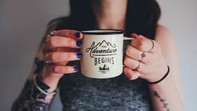 hands holding a mug saying the adventure begins for a post about how to start a sex blog