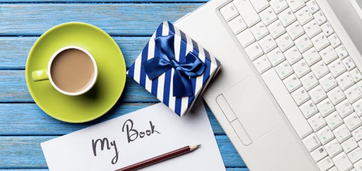image of laptop, cup of coffee, pen, open journal titled my book, and gift wrapped in white and blue paper with a blue ribbon showing different options for gifts for writers