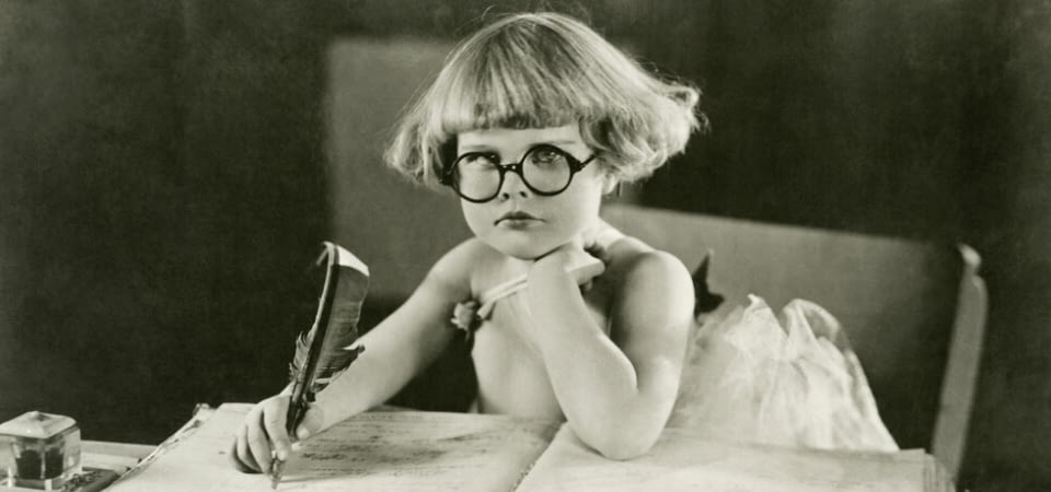 vintage photo of a young child holding a quill pen and frowning